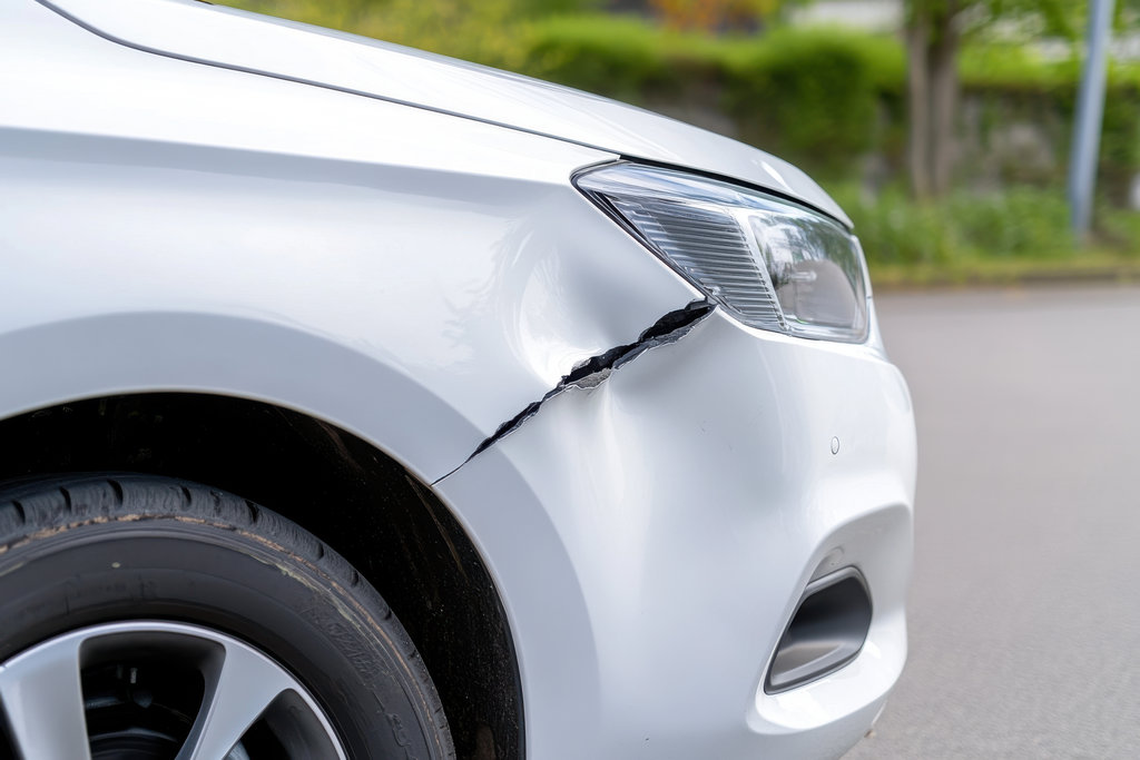 Close up of a large crack, dent on a white car fender, indicating collision damage, requiring repair.