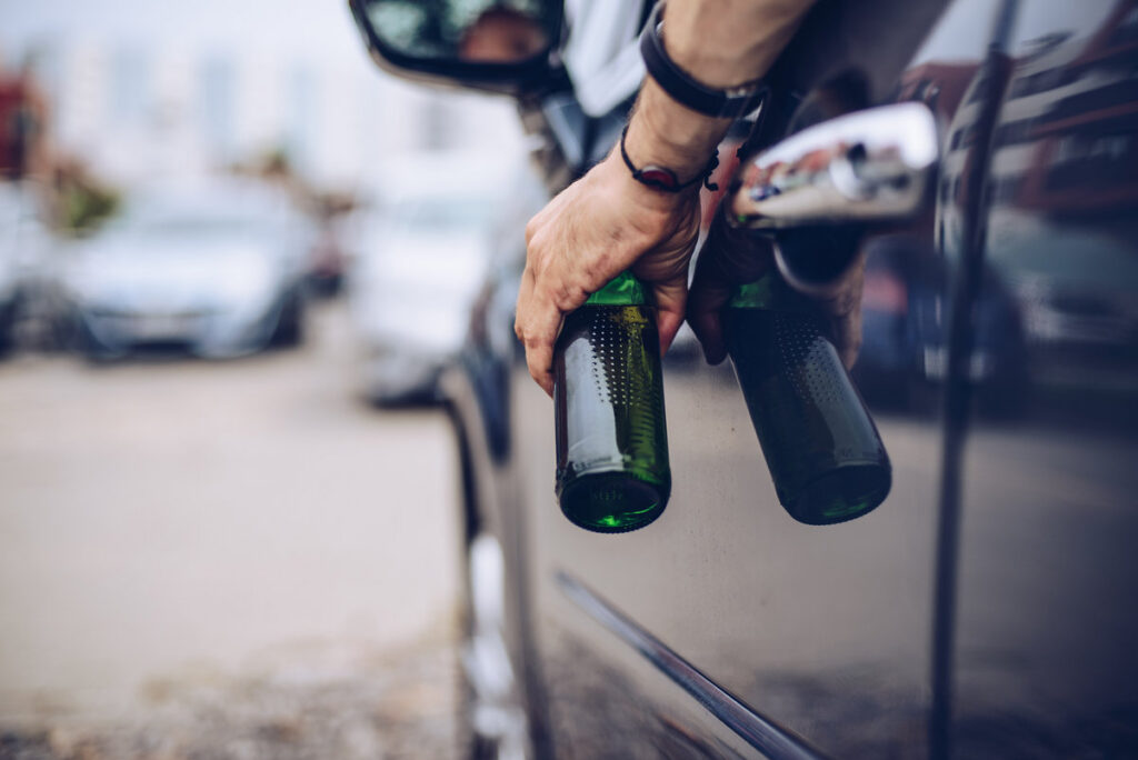Drunk driver drinking alcohol in car and holding beer bottle